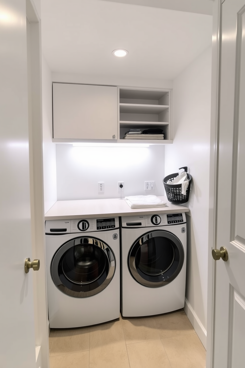 A small laundry room with efficient use of space. There are stacked washer and dryer units against one wall, with a countertop above for folding clothes. Task lighting is installed above the work areas to ensure adequate illumination. The walls are painted a soft white, and there are open shelves for storage of laundry supplies.