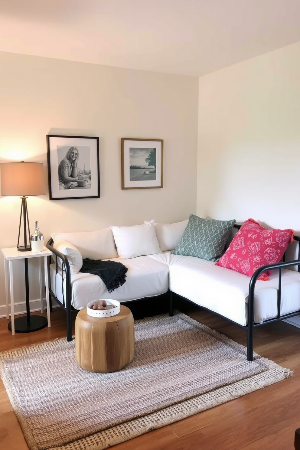 A cozy small living room featuring a corner sectional sofa in a soft gray fabric. A round wooden coffee table sits in front, adorned with a stack of books and a decorative bowl. In the opposite corner, a tall bookshelf is filled with plants and personal mementos. A floor lamp with a warm glow stands beside the sofa, creating an inviting reading nook.