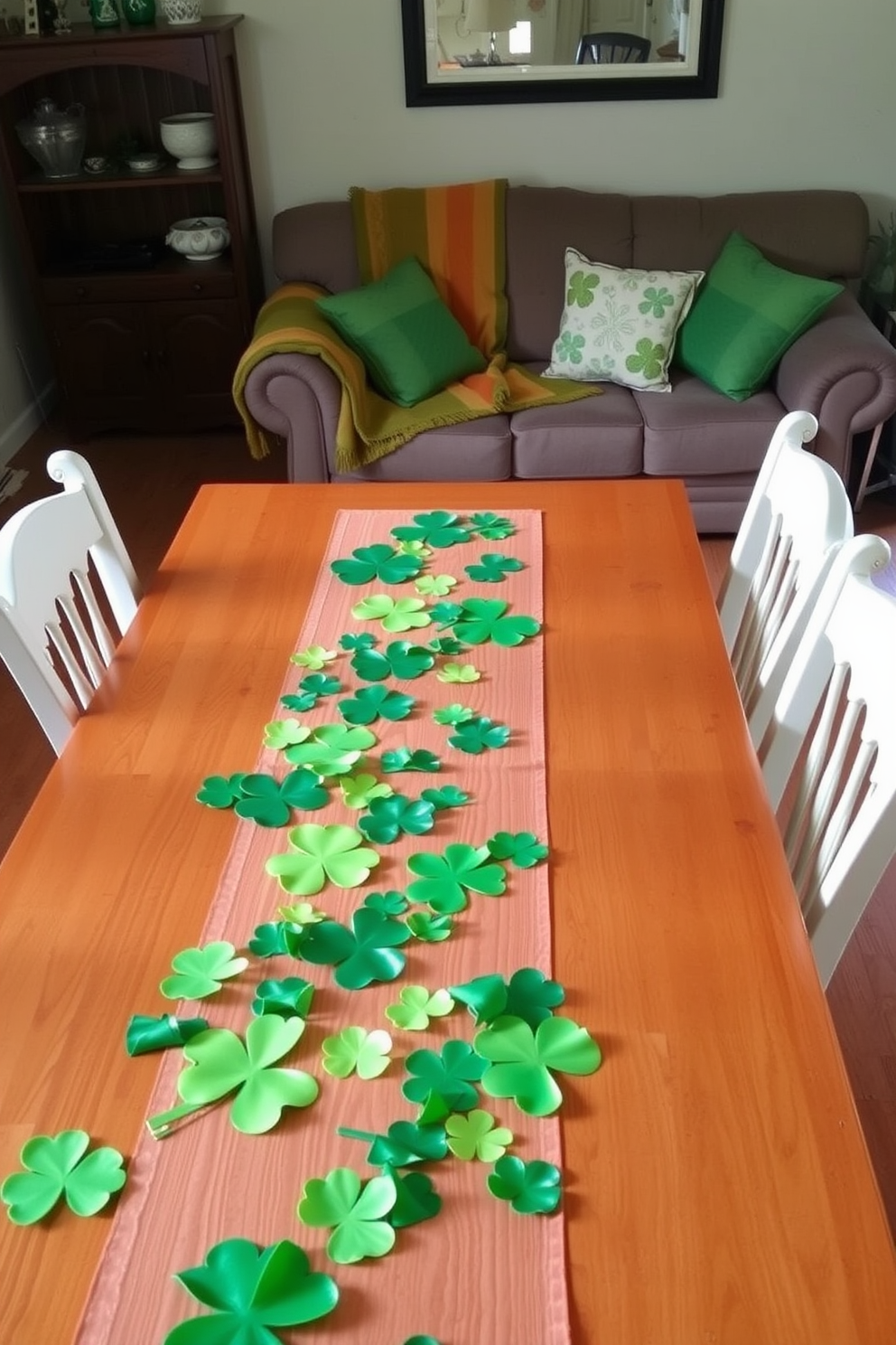 A festive table runner adorned with vibrant green clovers stretches across a polished wooden dining table. Surrounding the table are mismatched chairs, each featuring a unique design that adds character to the small living room. In the background, a cozy sofa is draped with a soft throw blanket in shades of green and gold. Decorative pillows with shamrock patterns are scattered across the sofa, enhancing the St. Patrick's Day theme.