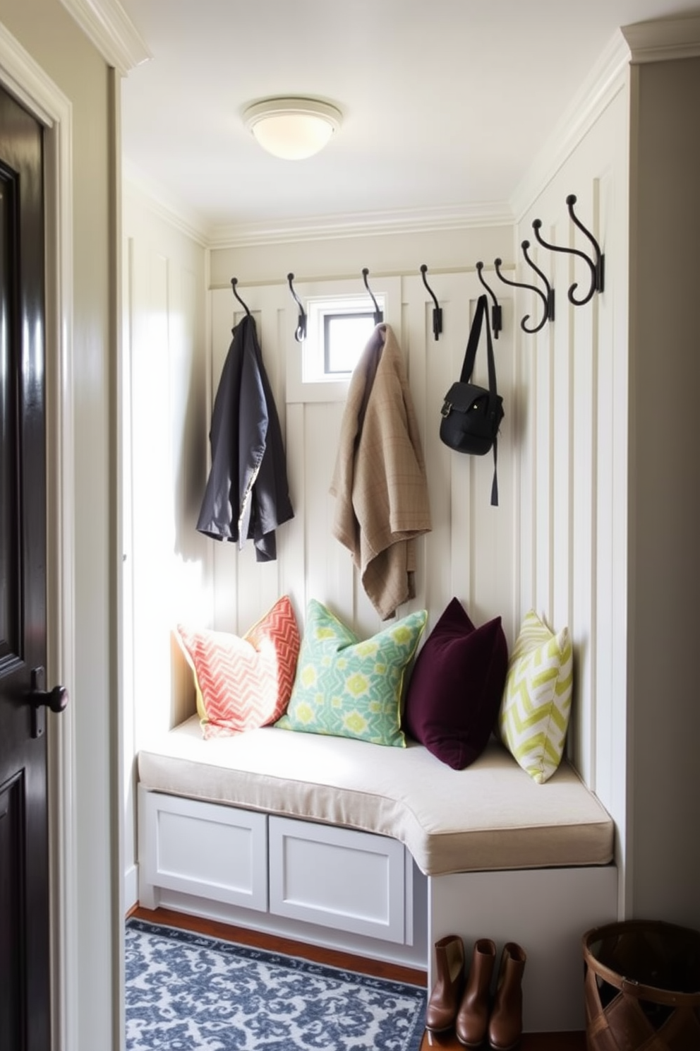 A cozy mudroom featuring a padded bench that combines comfort and style. The bench is upholstered in a soft fabric and is adorned with colorful throw pillows, providing a welcoming spot to sit and remove shoes. The walls are lined with hooks for hanging coats and bags, while a stylish area rug adds warmth to the space. Natural light floods in through a small window, enhancing the inviting atmosphere of this functional entryway.