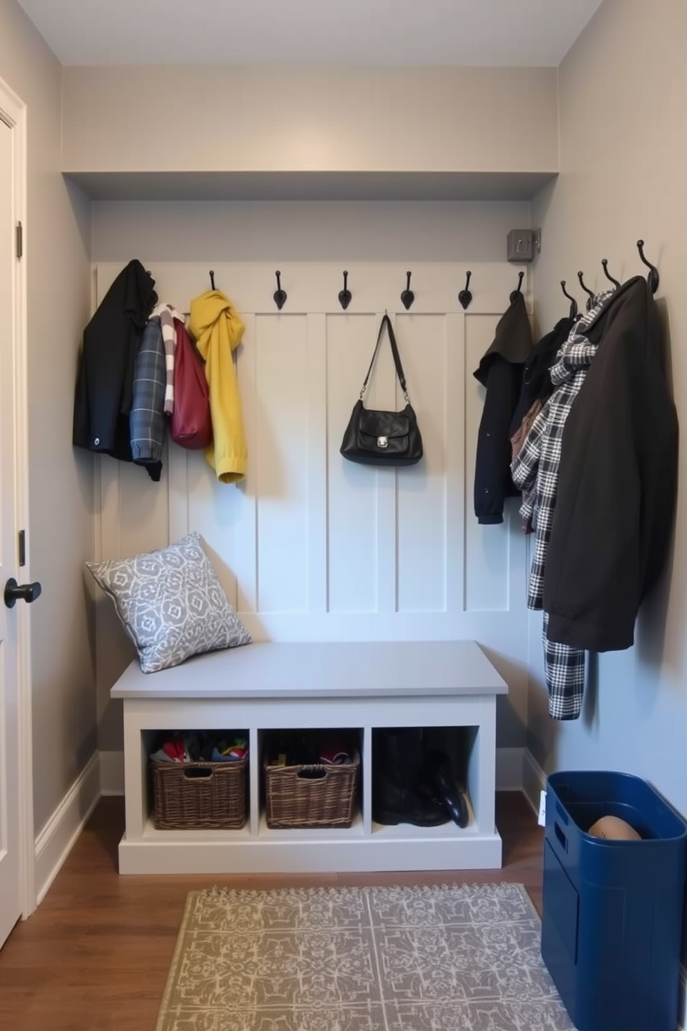 A cozy mudroom features a built-in bench with storage underneath and hooks on the wall for coats and bags. The walls are painted in a soft gray color, and a patterned rug adds warmth and texture to the space.