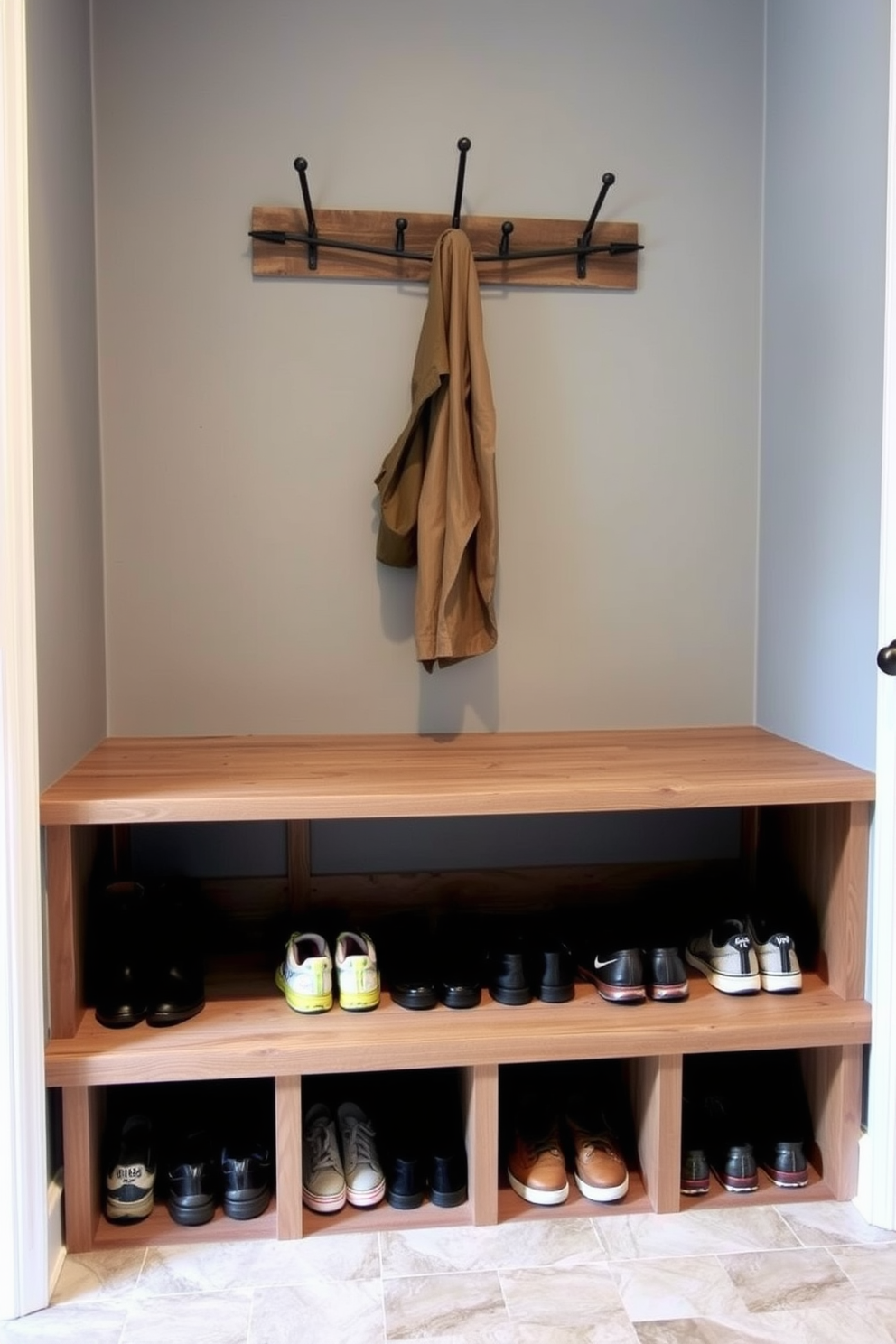 A cozy mudroom featuring wall hooks for coats and bags. The space is illuminated by natural light streaming through a small window, creating a welcoming atmosphere. The walls are painted in a soft gray tone, complemented by a durable wooden bench for seating. A stylish area rug adds warmth, while decorative baskets below the bench provide convenient storage.