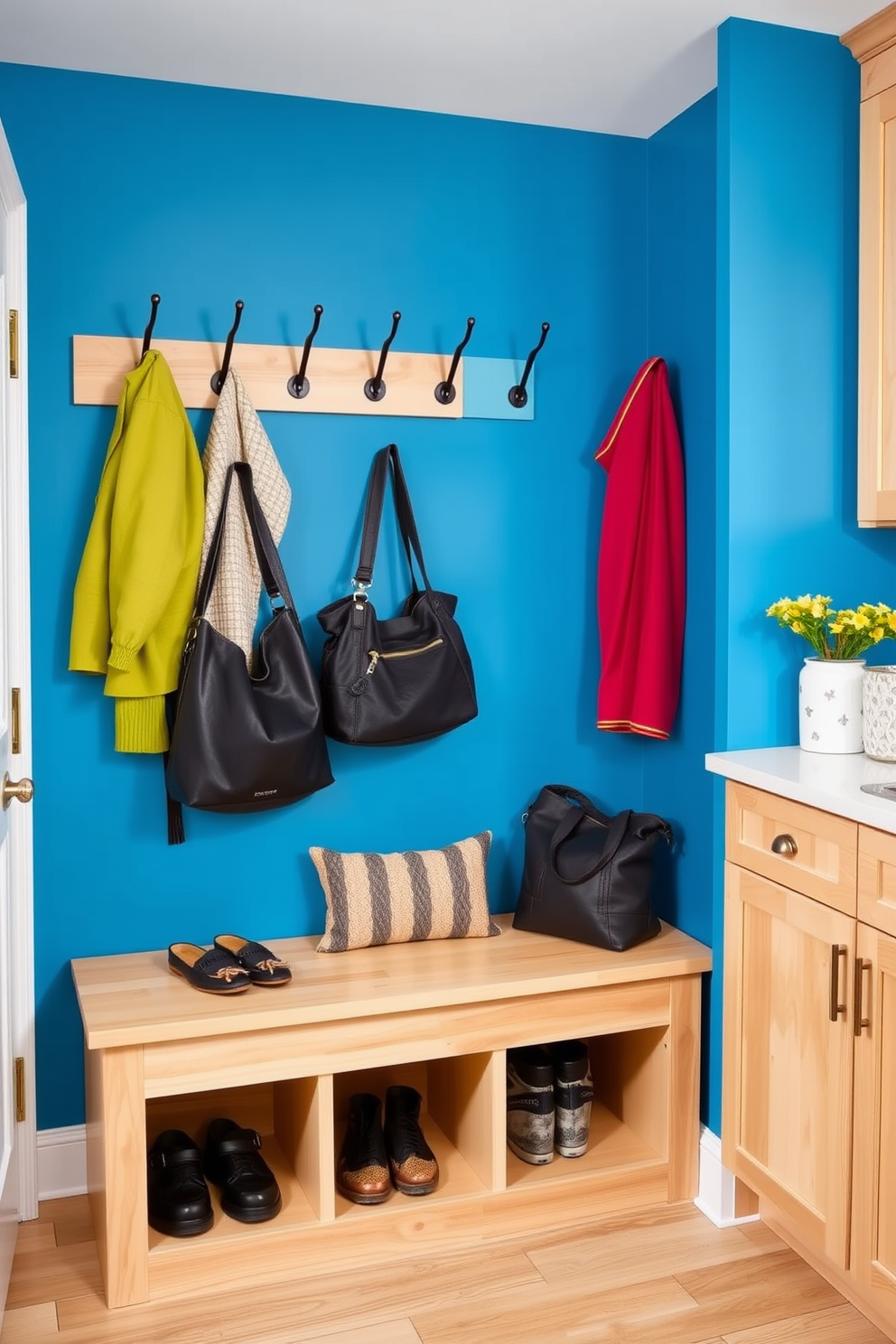 A vibrant accent wall painted in a bold hue adds a striking focal point to the space. The wall is adorned with hooks for coats and bags, enhancing both style and functionality. The small mudroom features a built-in bench with storage underneath for shoes and bags. Light wood cabinetry complements the colorful wall, creating a cheerful and inviting atmosphere.