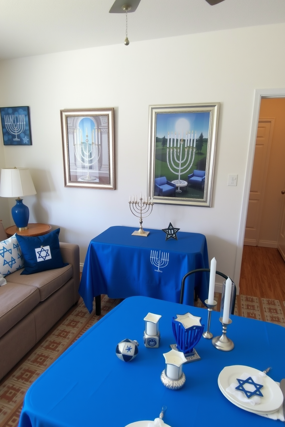 A cozy living room adorned with Hanukkah-themed art on the walls. The decor features blue and silver accents, with a small menorah placed on a coffee table surrounded by decorative dreidels. A compact dining area showcases a festive table setting with a vibrant blue tablecloth. Small decorative items like star of David napkin holders and candles enhance the Hanukkah spirit while maximizing the limited space.