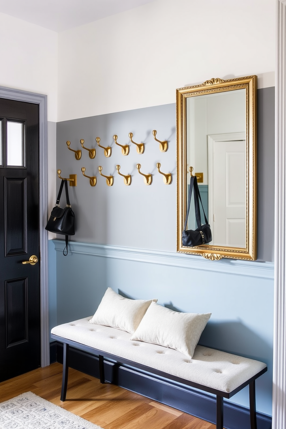 A stylish hallway featuring wall-mounted hooks for coats and bags. The hooks are made of brushed brass and are arranged in an artistic pattern along a soft blue accent wall. A cozy bench sits beneath the hooks, adorned with plush cushions in neutral tones. A large mirror with a decorative frame hangs above the bench, reflecting light and enhancing the space's openness.