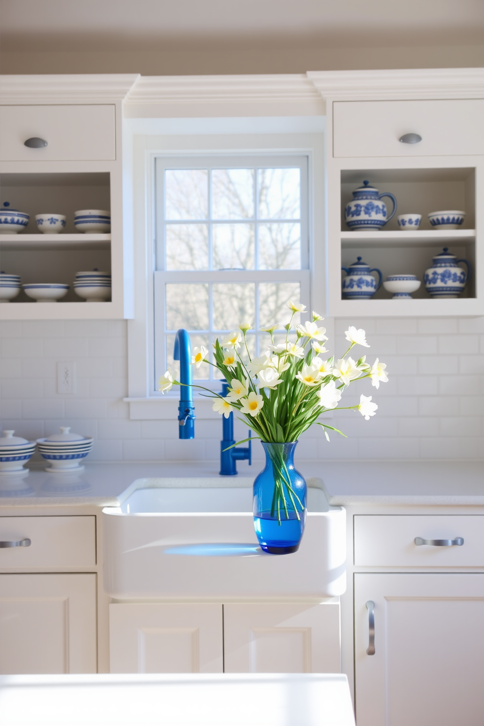 A bright and airy kitchen filled with natural light. The cabinetry is painted in a crisp white, complemented by blue and white ceramic accents displayed on open shelves. A large farmhouse sink sits beneath a window, with a stylish blue faucet adding a pop of color. Fresh spring flowers in a blue vase are arranged on the countertop, creating a cheerful focal point.