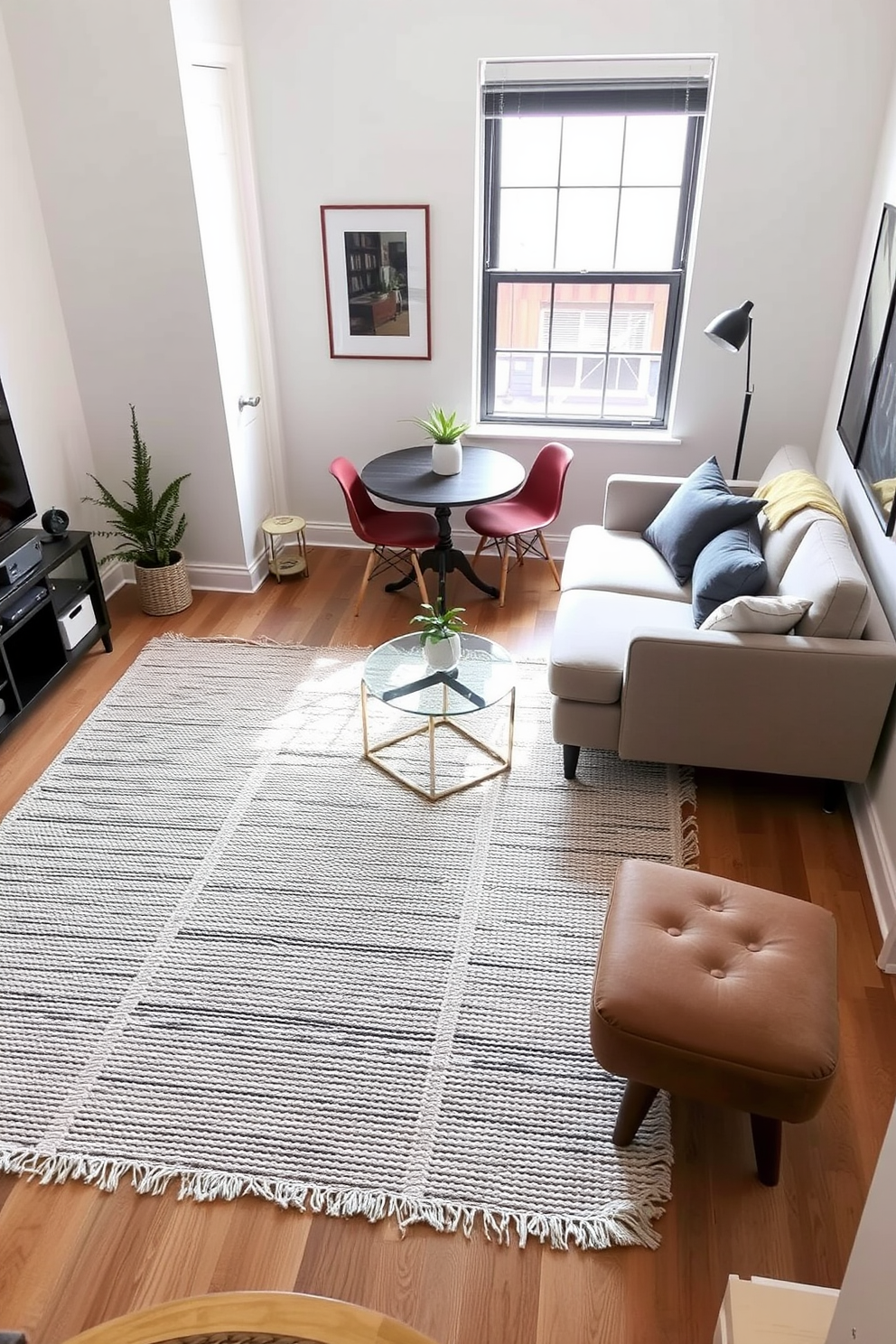 Create defined zones with rugs in a studio living room featuring a cozy seating area with a plush sectional sofa in a neutral tone. The area is anchored by a large textured area rug that adds warmth and delineates the space from a small dining nook with a round table and stylish chairs.