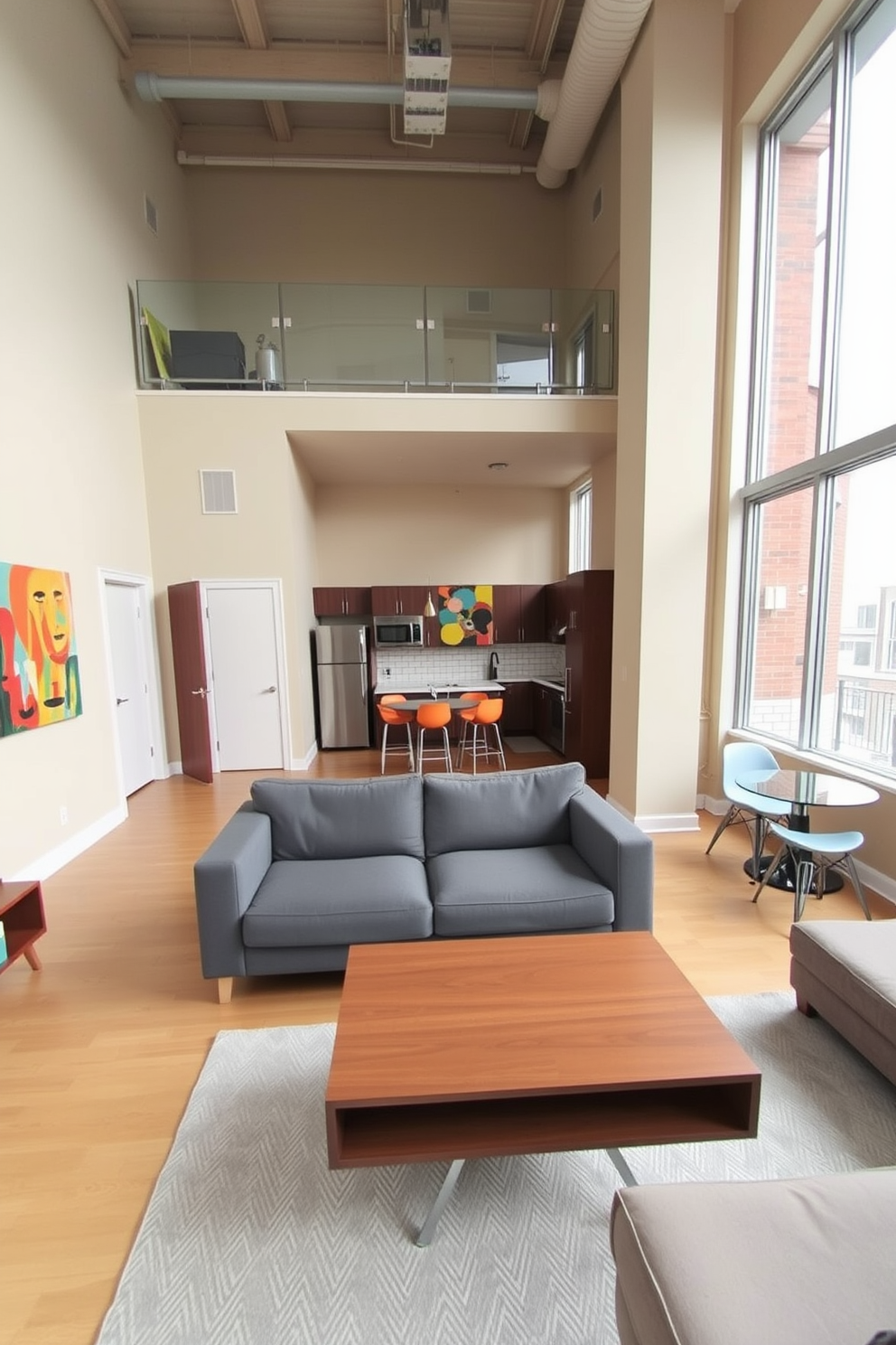 A spacious studio loft apartment featuring an open floor plan with high ceilings and large windows. The walls are painted in a soft beige, while the furniture includes a plush gray sofa and a sleek wooden coffee table, creating a cozy yet modern atmosphere. In the living area, a vibrant abstract painting adds a pop of color above the sofa. A small dining table with colorful chairs is placed near the kitchen, which boasts stainless steel appliances and a white subway tile backsplash.