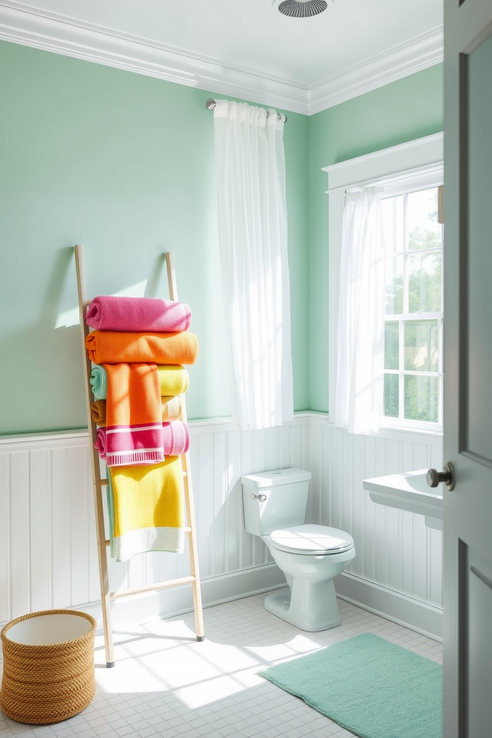 A bright and airy bathroom featuring a vibrant beach towel display. The towels are neatly arranged on a stylish ladder rack, showcasing a variety of colors and patterns that evoke a seaside vibe. The walls are painted in a soft seafoam green, complemented by white wainscoting. Natural light floods the space through a large window adorned with sheer white curtains, enhancing the cheerful atmosphere.