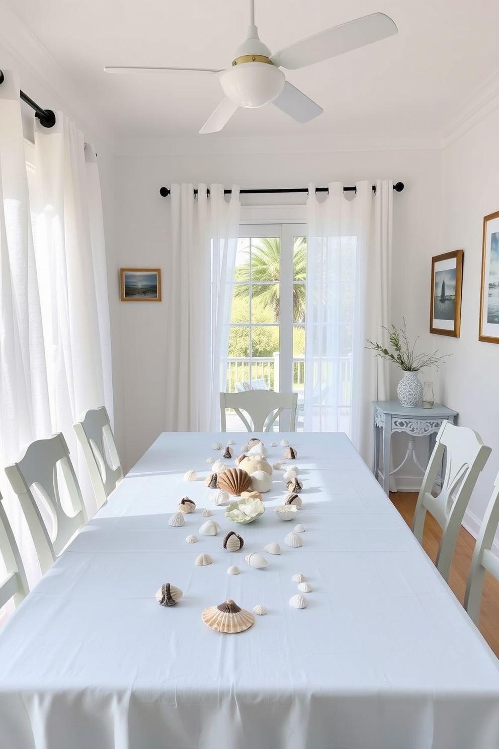 A bright and airy dining room inspired by summer beach vibes. The table is adorned with a light blue tablecloth, and seashells are scattered along the center as a natural centerpiece. Beach-themed decorations hang on the walls, including framed artwork of ocean scenes. Soft white curtains flutter gently in the breeze, allowing natural light to fill the space.