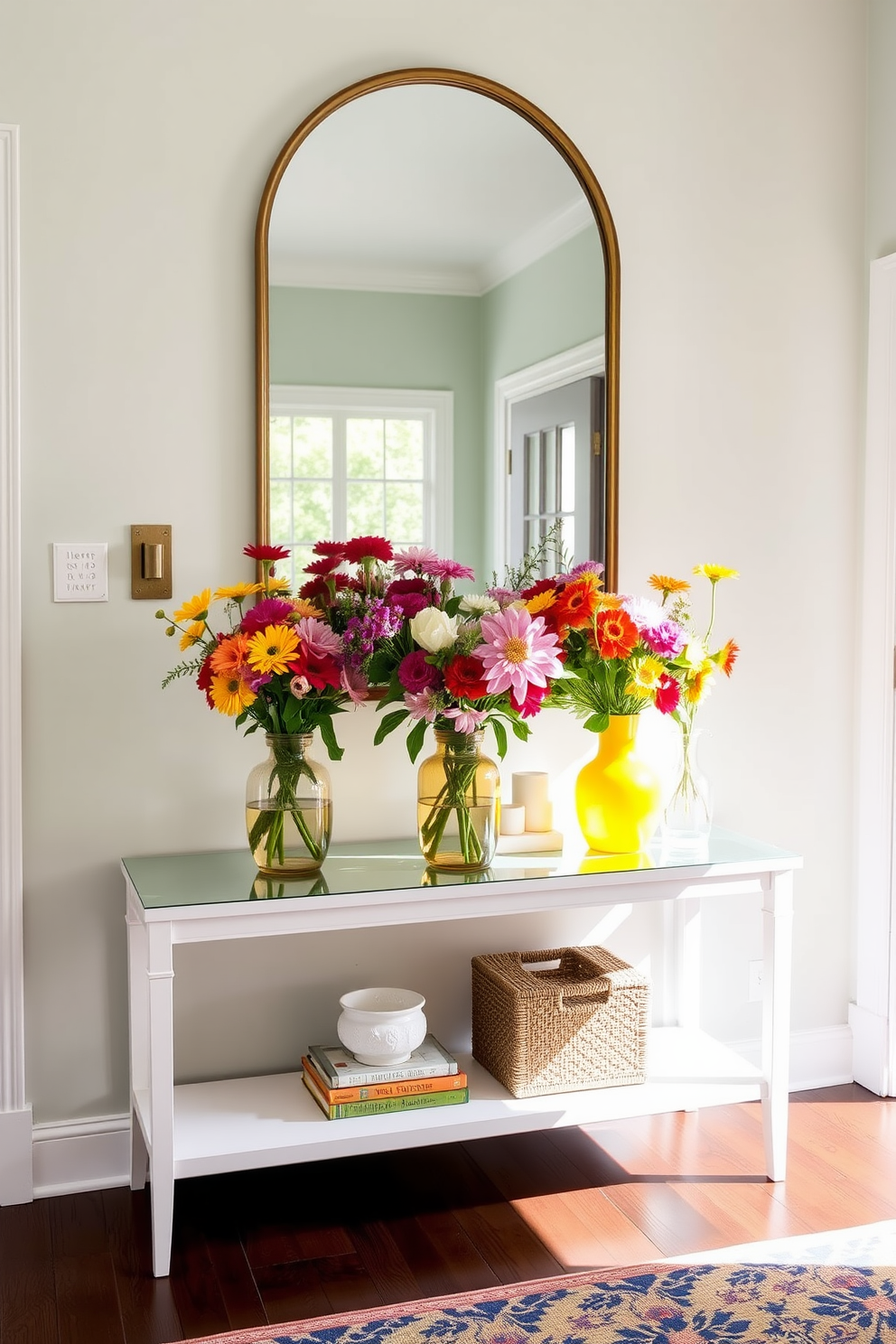 A bright and inviting summer entryway features a stylish console table adorned with vibrant flower arrangements in colorful vases. The walls are painted in a soft pastel hue, and a large mirror above the table reflects natural light, enhancing the cheerful atmosphere.