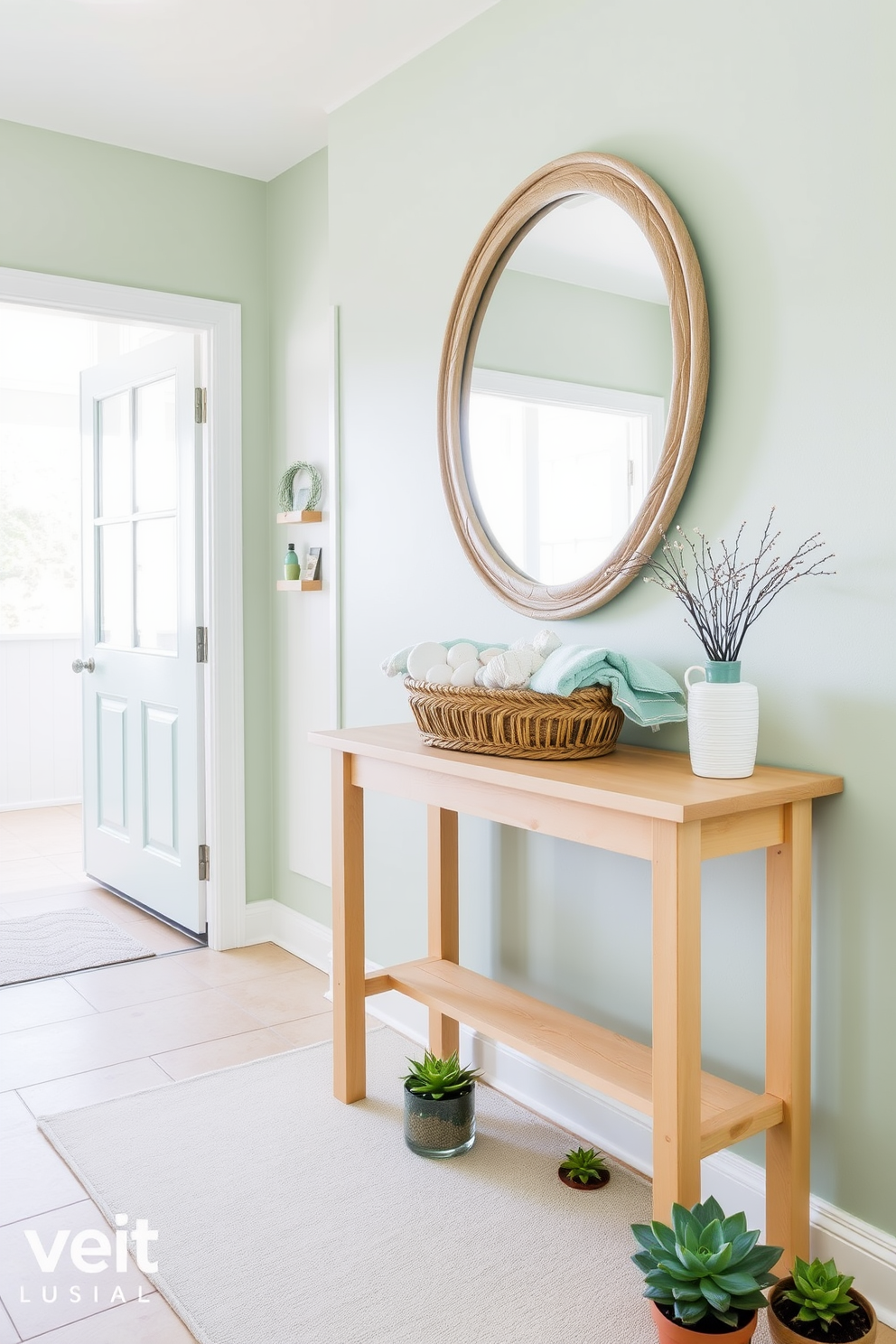 A bright and airy entryway features a light wood console table adorned with a woven basket filled with seashells and beach towels. Above the table, a large round mirror with a driftwood frame reflects the natural light streaming in from the nearby window. The walls are painted in a soft seafoam green, complementing the sandy beige floor tiles. A coastal-themed area rug with a subtle wave pattern lies beneath the table, while a few potted succulents add a touch of greenery to the space.