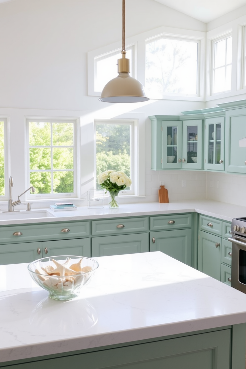 A bright and airy summer kitchen with a coastal theme. The cabinetry is painted in soft seafoam green, and the countertops are white with subtle gray veining. Seashells are artfully arranged in a glass bowl on the kitchen island. Natural light floods the space through large windows, enhancing the cheerful atmosphere.