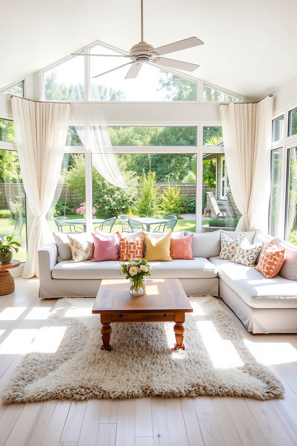 A bright and airy summer living room filled with natural light. Soft white curtains flutter gently in the breeze, framing large windows that overlook a vibrant garden. The space features a comfortable sectional sofa upholstered in light pastel colors, adorned with colorful throw pillows. A wooden coffee table sits at the center, surrounded by a plush area rug that adds warmth to the room.