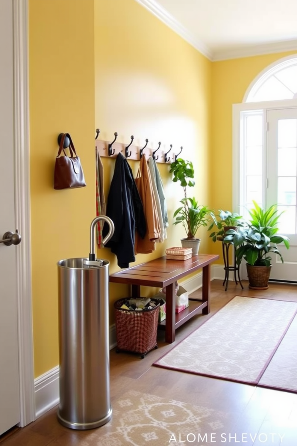 A bright and airy mudroom features a stylish umbrella stand made of brushed metal, elegantly positioned near the entrance. The walls are painted in a soft, inviting yellow, complemented by a cheerful patterned rug that adds a pop of color to the space. A row of hooks adorned with decorative accents hangs above a wooden bench, providing a practical yet stylish solution for storing jackets and bags. Natural light floods the room through a large window, illuminating potted plants that add a touch of greenery to the decor.