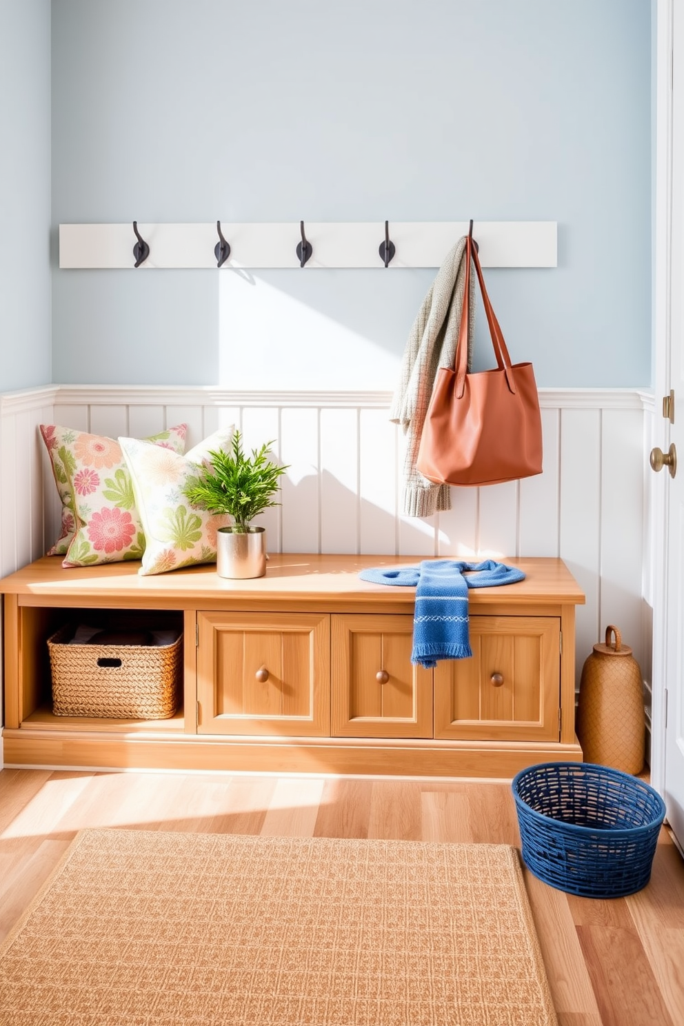 A bright and airy mudroom features a combination of natural wood and soft pastel colors. A bench with storage underneath is positioned against the wall, adorned with colorful cushions and a small indoor plant in a decorative pot beside it. The walls are painted in a light blue hue, complemented by white wainscoting. Hooks for coats and bags are mounted above the bench, and a patterned rug lies on the floor, adding warmth to the space.