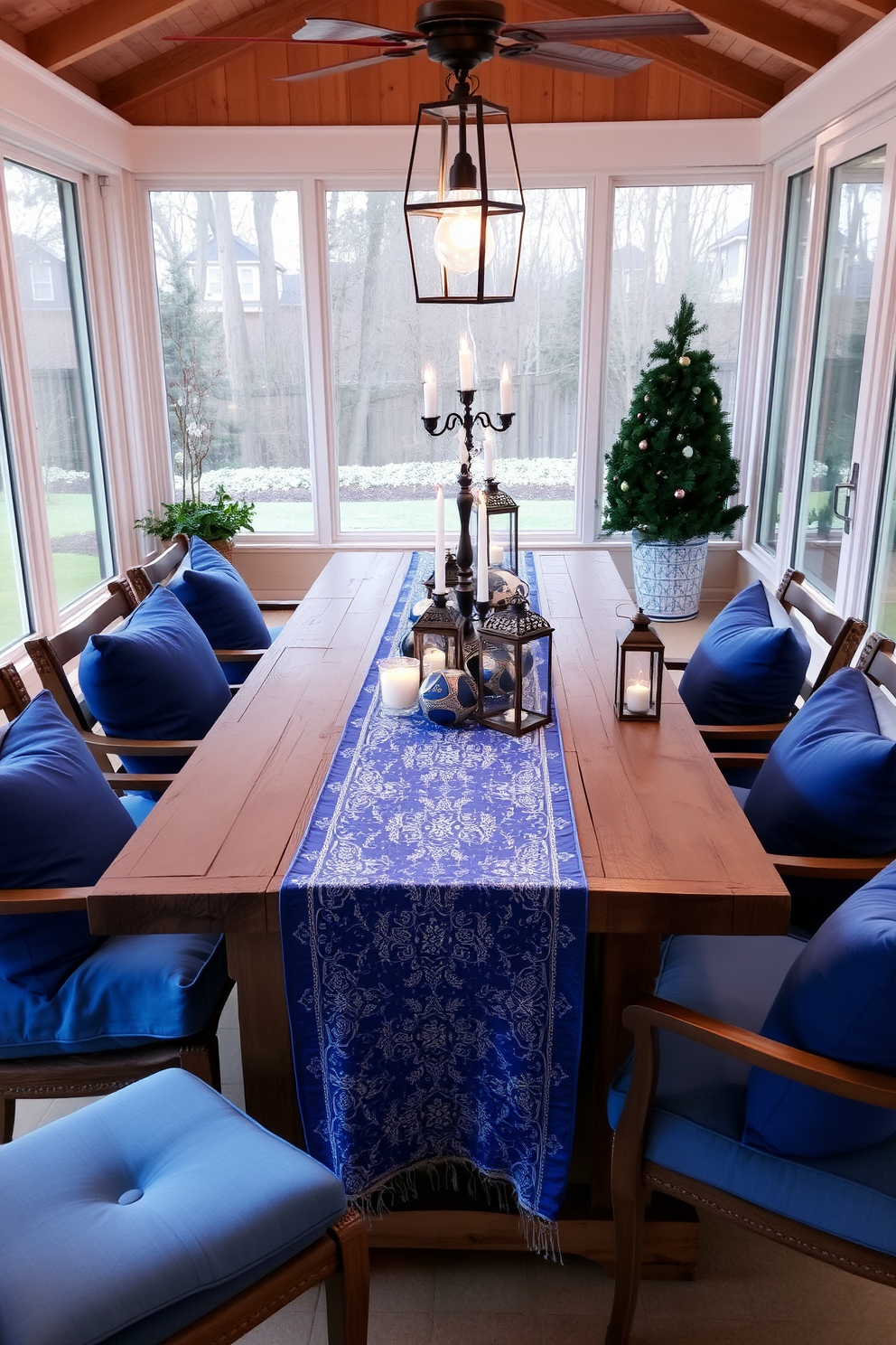 A sunroom adorned with Hanukkah-themed artwork on the walls creates a festive atmosphere. The artwork features vibrant blues and golds, showcasing traditional symbols like menorahs and dreidels. Cozy seating arrangements are complemented by soft, warm textiles in shades of blue and silver. Decorative elements such as string lights and festive garlands enhance the celebratory spirit of the space.