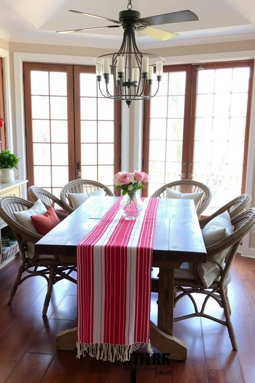 A sunlit sunroom features a red and white striped table runner draped elegantly across a rustic wooden dining table. Surrounding the table are comfortable wicker chairs adorned with plush cushions, creating a cozy atmosphere for Valentine's Day celebrations.