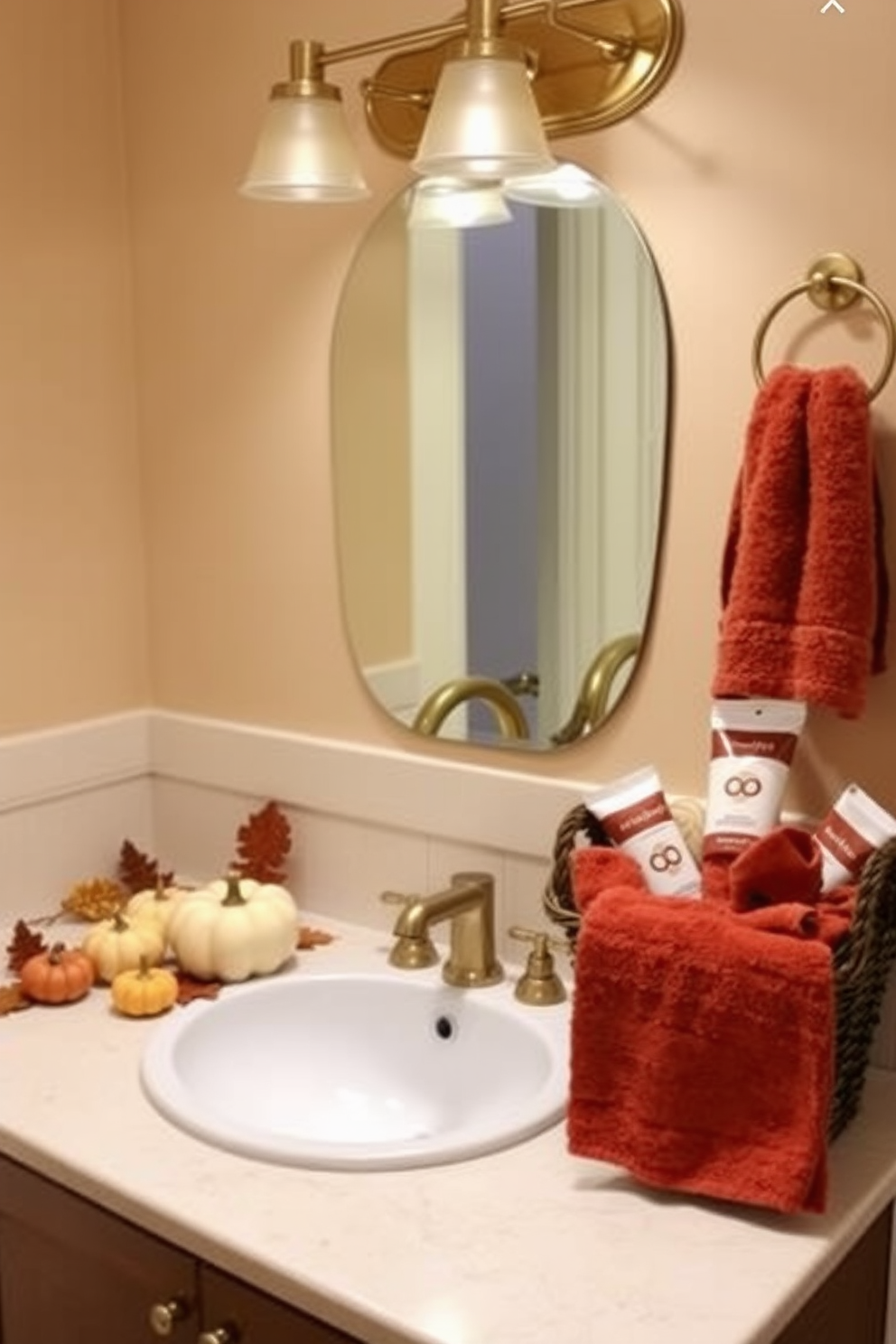 A cozy Thanksgiving bathroom setting featuring brushed gold fixtures that add a warm touch. The space includes autumn-themed decorations such as small pumpkins and dried leaves arranged around the sink area. The walls are adorned with soft beige tones, complemented by plush towels in rich, earthy colors. A decorative basket filled with seasonal toiletries sits beside the vanity, enhancing the festive atmosphere.