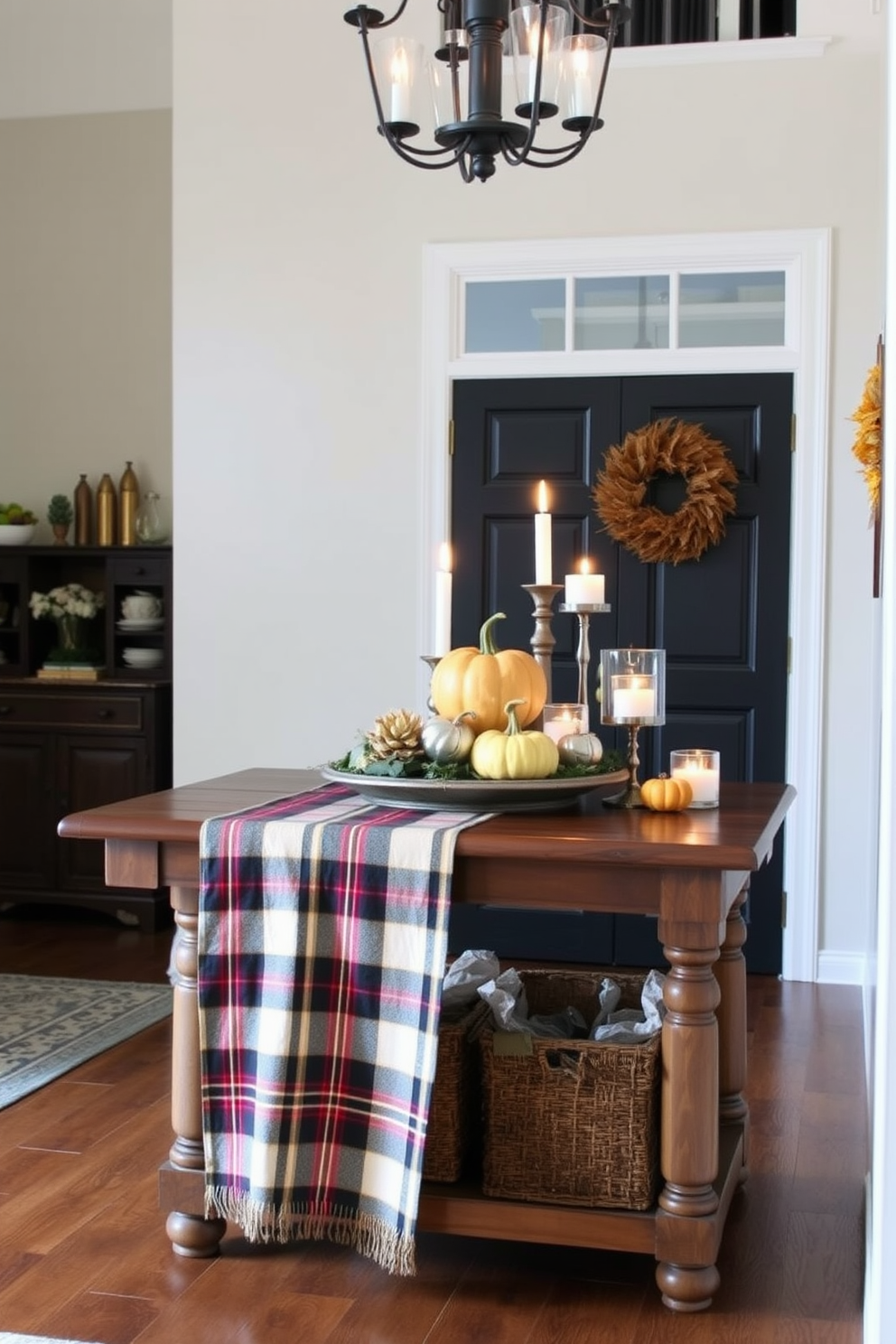 A warm and inviting entryway features a plaid tablecloth draped over a rustic wooden console table. On top of the table, there are decorative pumpkins, candles in varying heights, and a vibrant autumn wreath hanging on the wall.