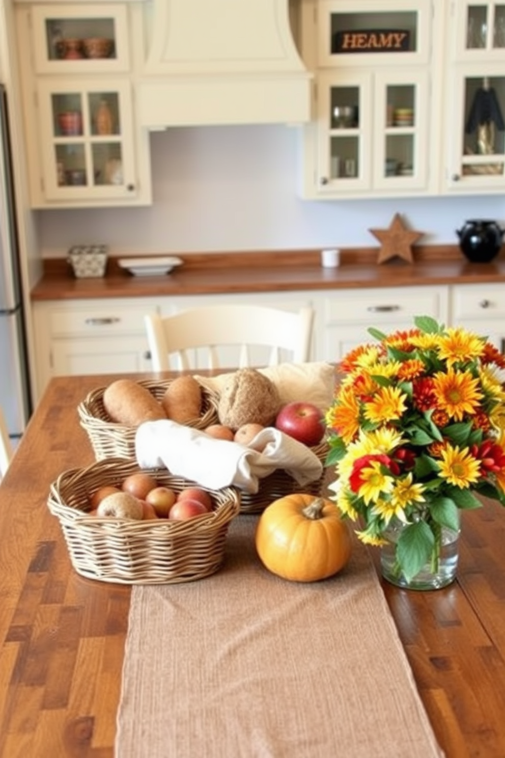 A warm and inviting kitchen setting for Thanksgiving. The table is adorned with a rustic table runner, and woven baskets filled with fresh bread and seasonal fruits are placed at the center. The cabinets are painted in a soft cream color, complementing the rich wooden countertops. A bouquet of autumn flowers sits in a vase on the side, adding a touch of color to the cozy atmosphere.