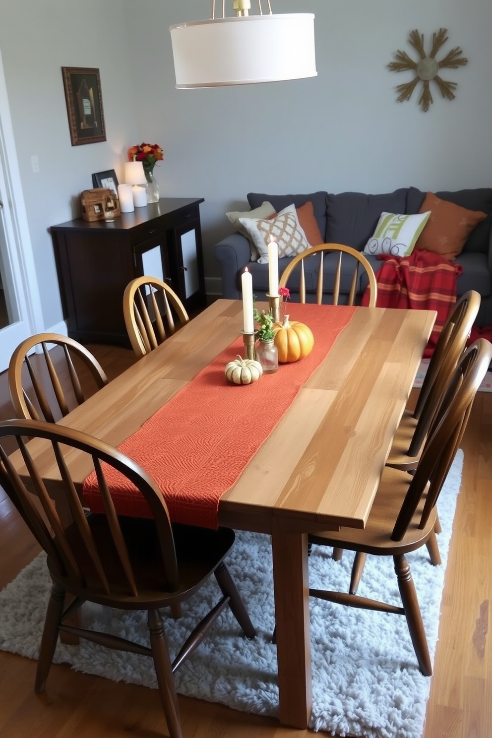 A cozy dining table adorned with an earthy toned table runner that complements the autumnal theme. Surrounding the table are mismatched wooden chairs, each with a unique design, creating a warm and inviting atmosphere. In the small living room, a plush area rug anchors the space, while decorative pillows in warm hues are scattered across a comfortable sofa. A few carefully arranged candles and a small vase with seasonal flowers add a touch of charm to the room.