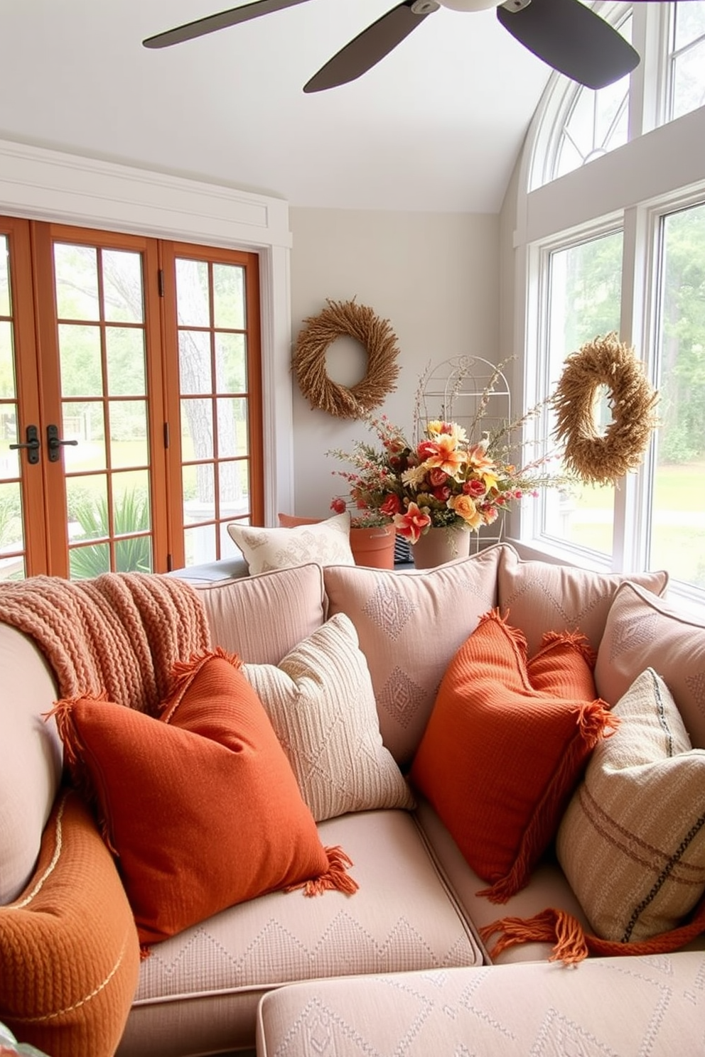 A cozy sunroom filled with comfortable seating adorned with warm, textured fabrics. Soft throw pillows in autumn hues are scattered across a plush sectional sofa, inviting relaxation and conversation.