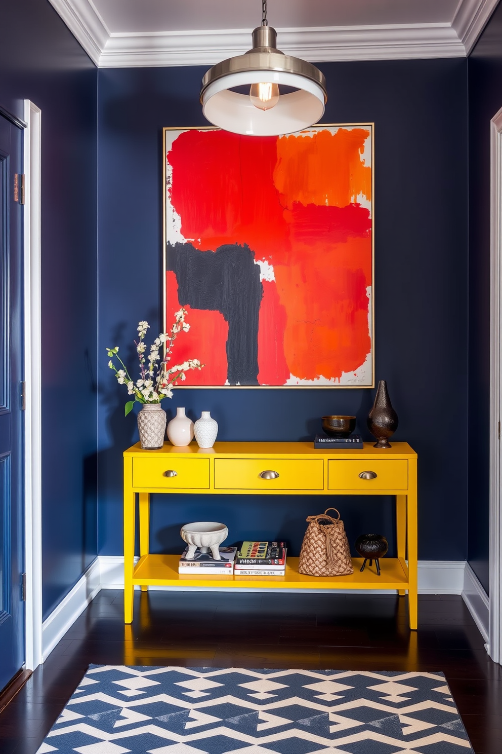 A striking townhouse entryway featuring bold colors that create a dramatic effect. The walls are painted in a deep navy blue, complemented by a vibrant yellow console table adorned with decorative items. A large abstract artwork in reds and oranges hangs above the table, drawing attention and adding energy to the space. The floor is covered with a geometric patterned rug that ties the color scheme together, while a stylish pendant light illuminates the area.