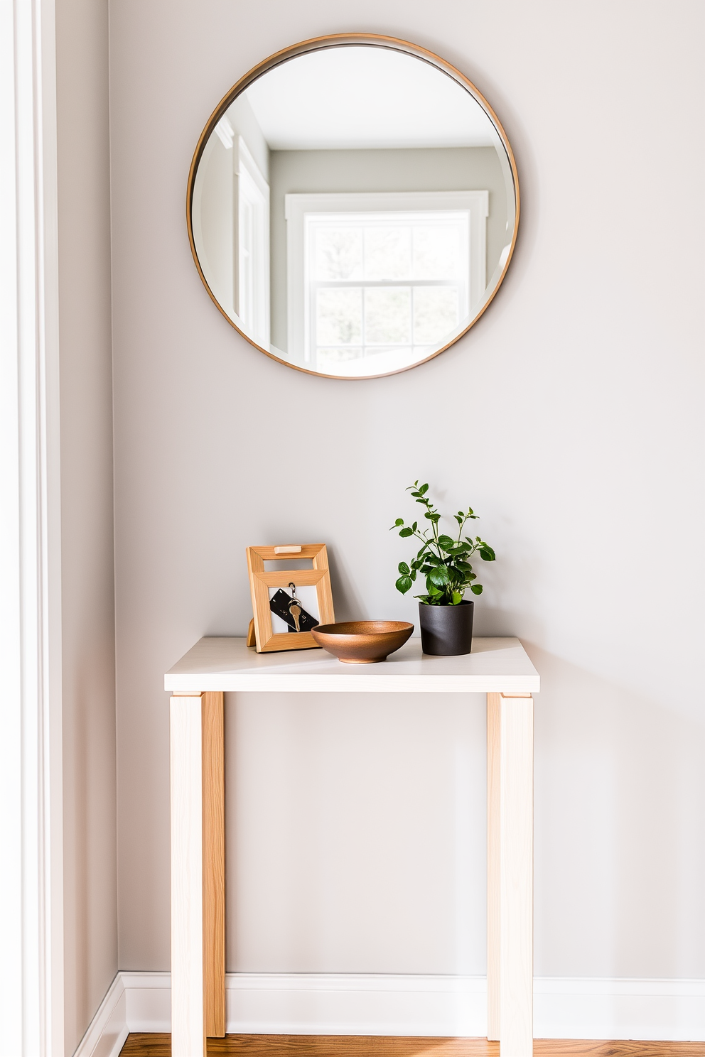 A narrow table for keys and essentials is positioned against the wall in a stylish townhouse entryway. The table features a sleek design with a light wood finish and is adorned with a small decorative bowl for storing keys and a framed photo for a personal touch. Above the table, a round mirror with a minimalist frame reflects the space, enhancing the natural light. The walls are painted in a soft gray hue, and a small potted plant sits on the table, adding a touch of greenery to the entryway.