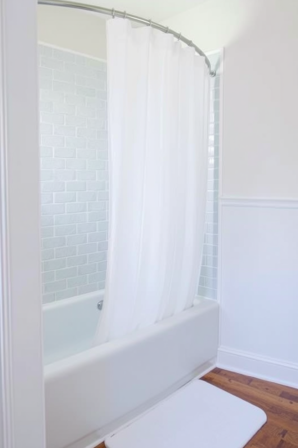 A serene bathroom space featuring a tub shower combo with a curved shower curtain that creates soft lines. The walls are adorned with light blue tiles, and the floor boasts a warm wooden finish that adds a touch of elegance.