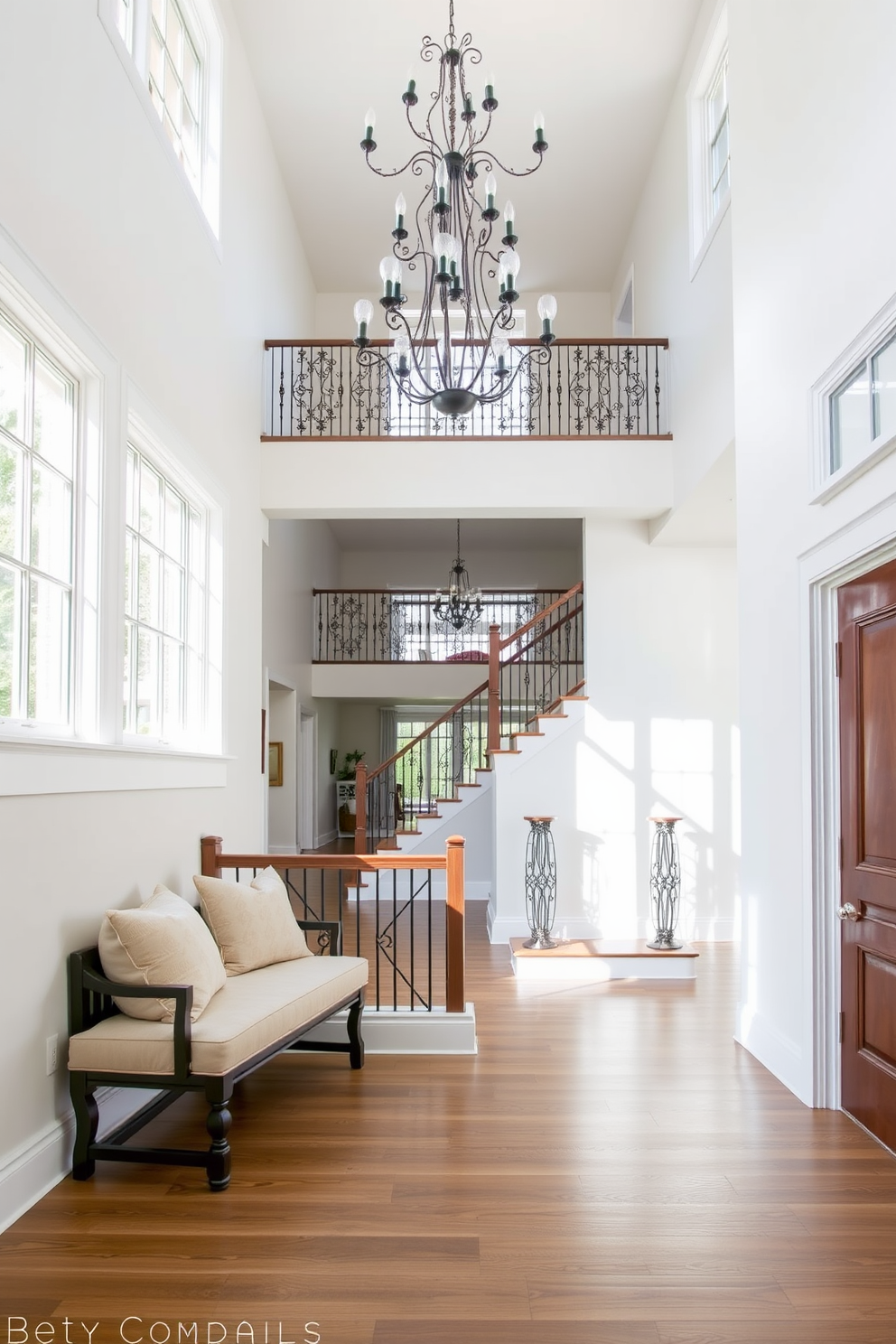 A welcoming bench for functional seating is placed against the wall in a bright entryway. The bench features plush cushions and is accompanied by decorative pillows to enhance comfort and style. The two story foyer design showcases a grand chandelier hanging from the high ceiling. Large windows on either side allow natural light to flood the space, highlighting the elegant staircase with intricate railings.