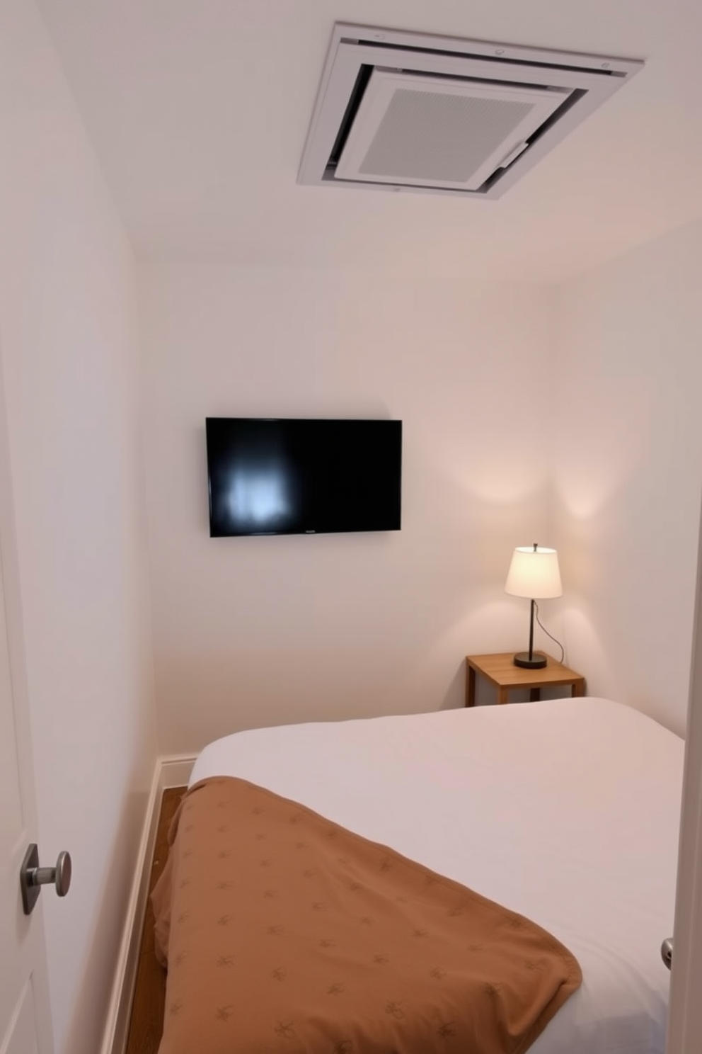 A cozy very small bedroom featuring a wall-mounted TV across from a compact bed with soft linens. The walls are painted in a light neutral color, creating an airy feel, while a small bedside table holds a stylish lamp.