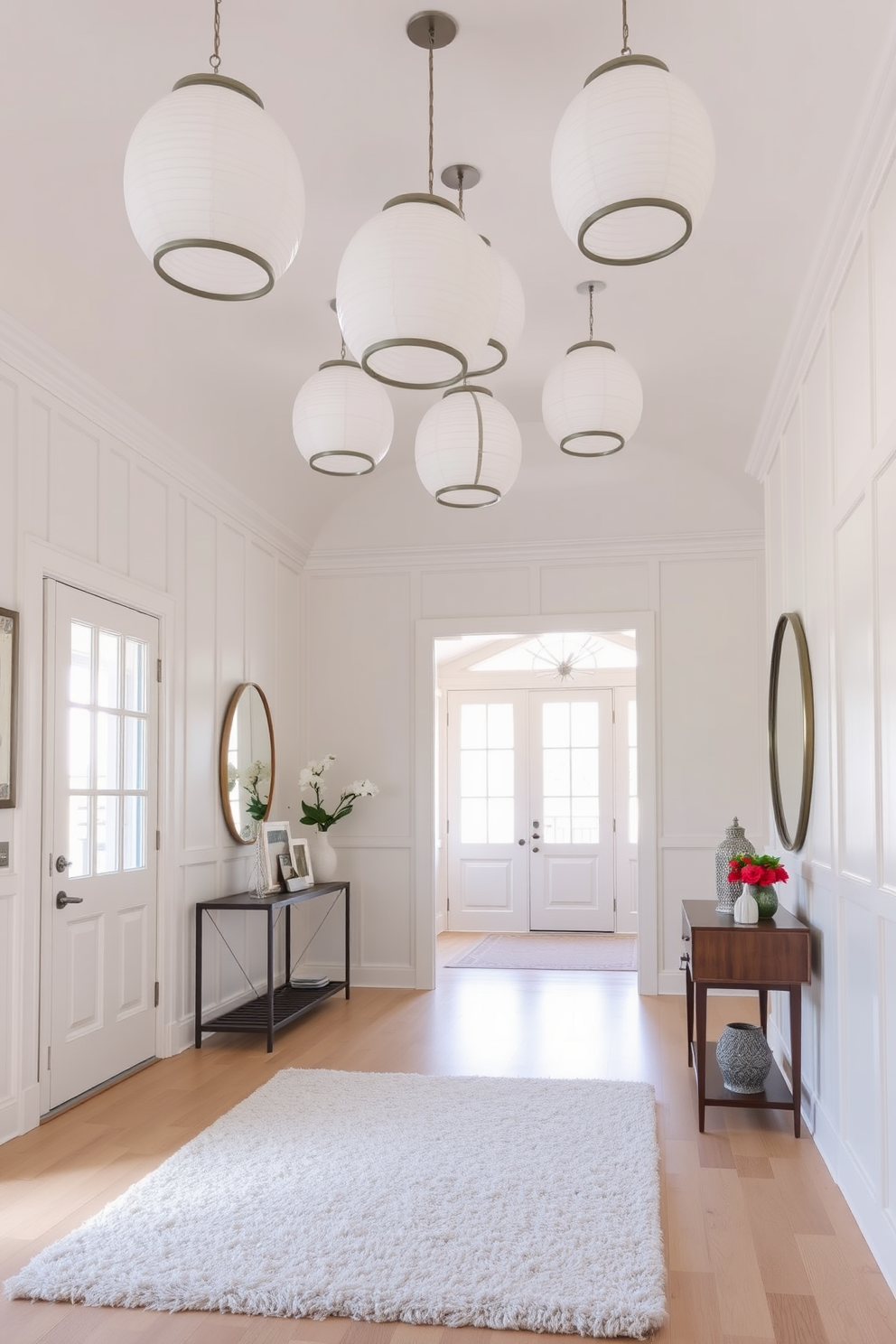 A bright and airy foyer features a sleek white console table against the wall. On the table, a collection of white ceramic vases in varying heights creates a clean and cohesive aesthetic. The walls are painted in a soft white hue, enhancing the sense of openness. A large round mirror hangs above the console, reflecting natural light and adding depth to the space.