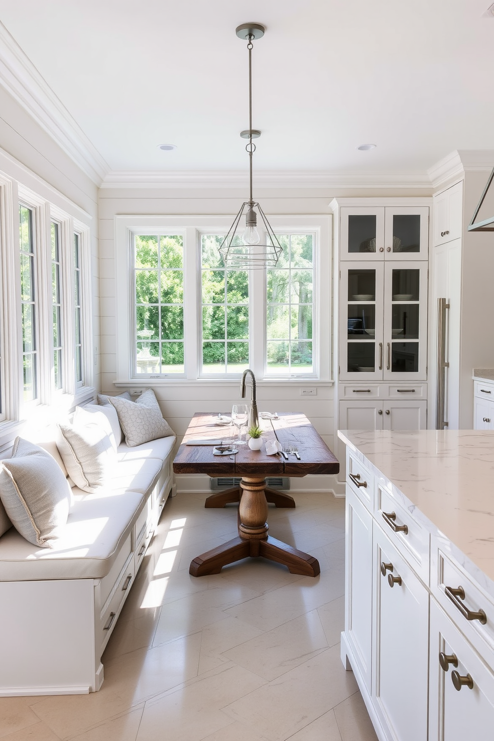 A built-in banquette with plush cushions creates a cozy dining space in the corner of the kitchen. The surrounding walls are adorned with soft white shiplap, and a rustic wooden table sits at the center, surrounded by elegant pendant lights. The white kitchen features sleek cabinetry with brushed nickel hardware and a spacious island for food preparation. Large windows allow natural light to flood the space, highlighting the marble backsplash and polished quartz countertops.