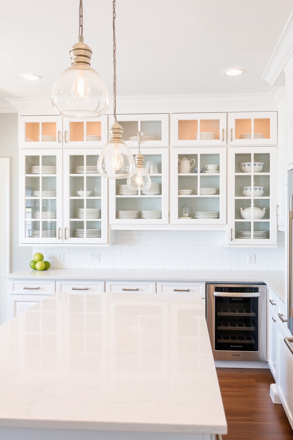 A minimalist kitchen design featuring sleek cabinetry with a high-gloss white finish. The space includes a large central island with a waterfall countertop made of white quartz, complemented by subtle pendant lighting above. The walls are painted in a soft white hue, enhancing the airy feel of the room. Stainless steel appliances are seamlessly integrated into the cabinetry, maintaining a clean and uncluttered aesthetic.