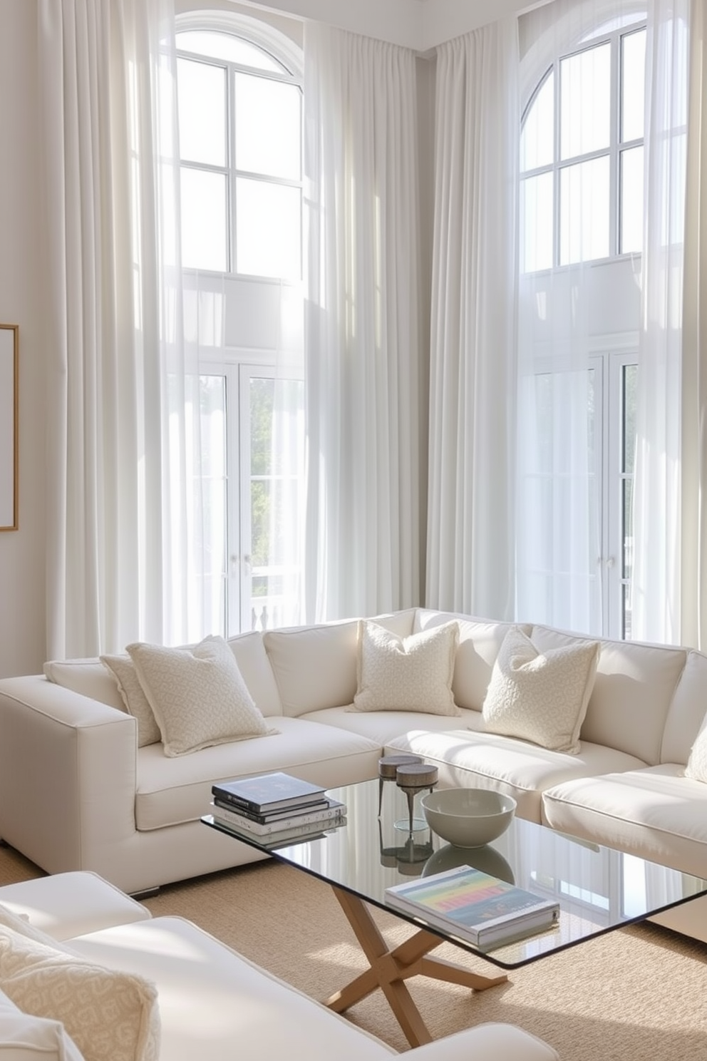 Elegant white drapes frame the large windows, allowing soft, diffused light to fill the room. The living space features a plush white sectional sofa, accented with textured throw pillows in shades of cream and beige. A sleek glass coffee table sits in the center, topped with a stack of art books and a small decorative bowl. The walls are adorned with subtle artwork, enhancing the airy atmosphere of the room.