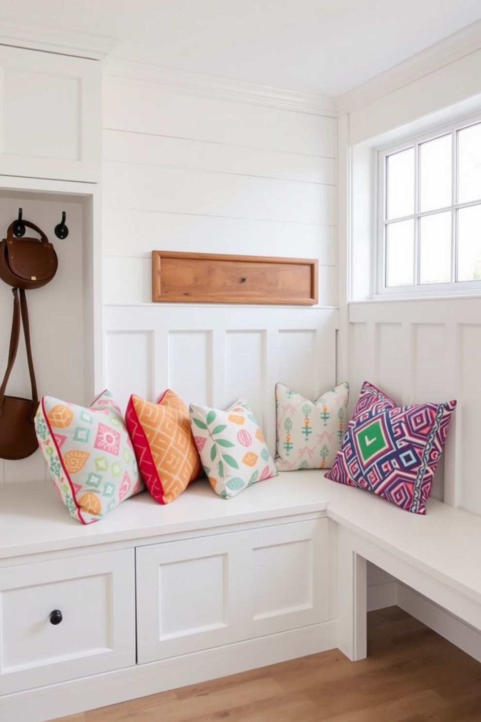 Cozy bench with colorful cushions. The bench is positioned against the wall with a backdrop of shiplap paneling, and vibrant throw pillows in various patterns and colors add warmth and comfort. White mudroom design ideas. The space features built-in storage cubbies, a sleek white bench for seating, and hooks for hanging coats, all complemented by a bright and airy atmosphere created by large windows.