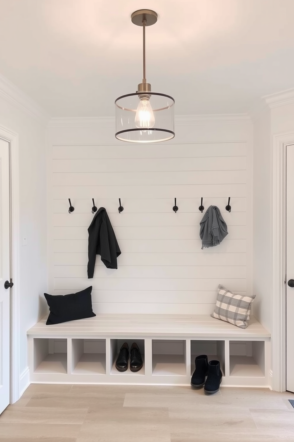 A bright and airy mudroom features white cabinetry that provides organized storage for shoes and outdoor gear. The space is accented with a stylish bench and hooks for coats, creating a functional and welcoming entryway. The walls are painted in a soft gray hue, complementing the white cabinetry and enhancing the natural light coming through the windows. A durable, patterned rug adds warmth and texture to the floor, making the mudroom both practical and inviting.