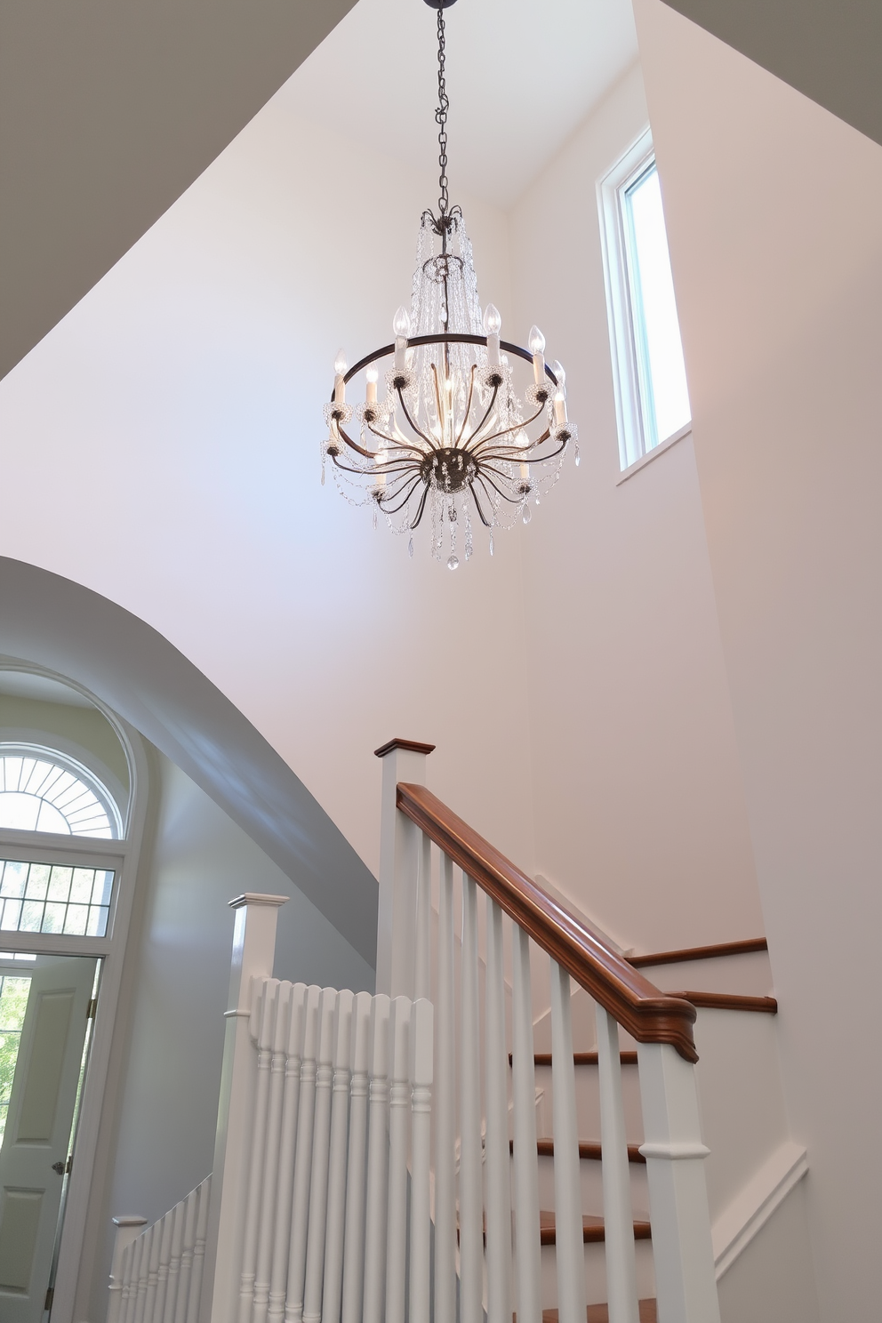 A stunning white staircase ascends gracefully, illuminated by a bold chandelier that commands attention from above. The staircase features sleek white balusters and a polished wooden handrail, creating an elegant contrast against the bright backdrop.