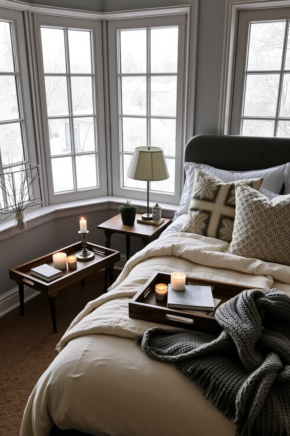 A cozy winter bedroom retreat featuring a plush king-sized bed dressed in layered white and gray blankets. Flanking the bed are two wooden nightstands adorned with scented candles, creating a warm and inviting atmosphere. The walls are painted in a soft blue hue, complementing the snowy landscape visible through the large window. A chunky knit throw is draped over the foot of the bed, while a stylish area rug adds texture and comfort underfoot.