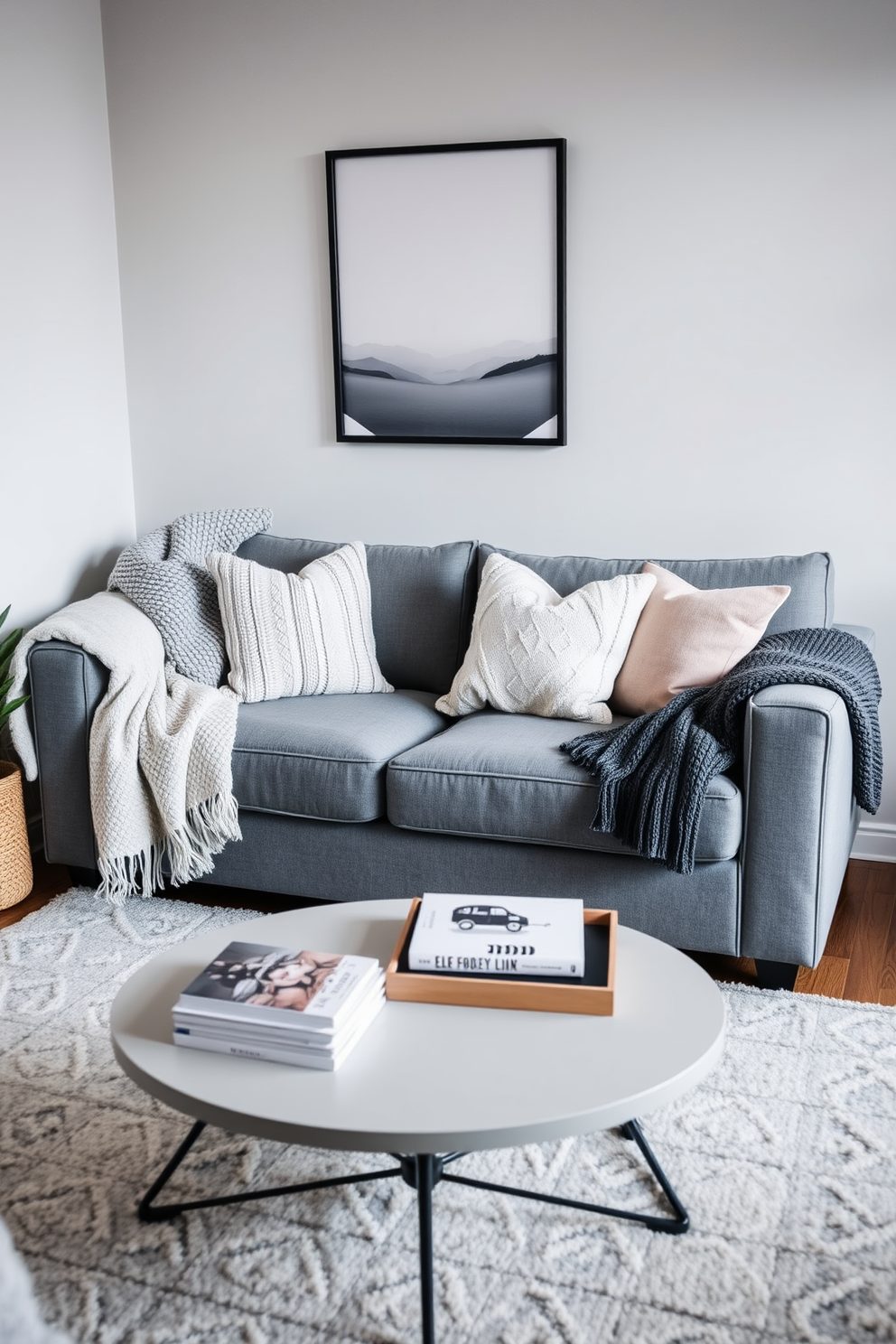 A cozy winter-themed living room perfect for small spaces. The room features a plush gray sofa adorned with knitted throw blankets and decorative pillows in soft, muted tones. A compact coffee table sits in front of the sofa, topped with a stack of books and a decorative tray. In the corner, a small indoor plant adds a touch of freshness and life to the space.