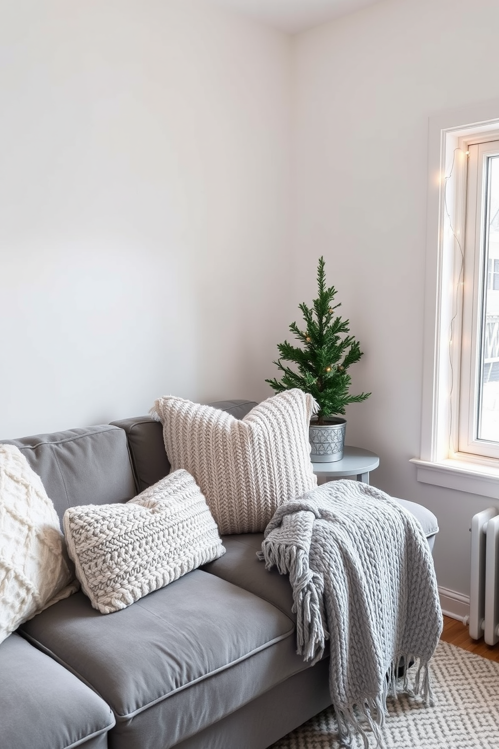 A cozy winter small space living room. A plush gray sofa is adorned with warm, textured throw pillows, and a small round side table is placed beside it for functionality. The walls are painted in a soft white to enhance the natural light, while a chunky knit blanket drapes over the arm of the sofa. A small evergreen tree in a decorative pot adds a touch of winter charm, and a set of twinkling fairy lights is strung along the window for a warm ambiance.