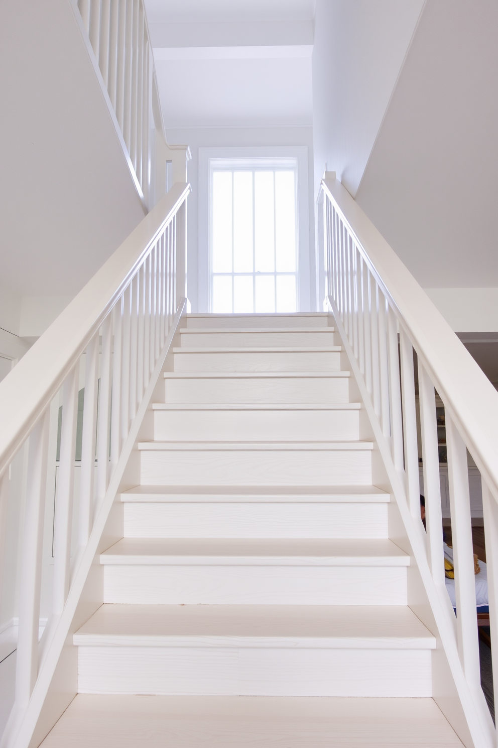 A whitewashed wooden staircase leads up to a bright and airy space, embodying a coastal aesthetic. The steps are adorned with subtle grain patterns, and the banister features a sleek, minimalist design that complements the overall lightness of the space.