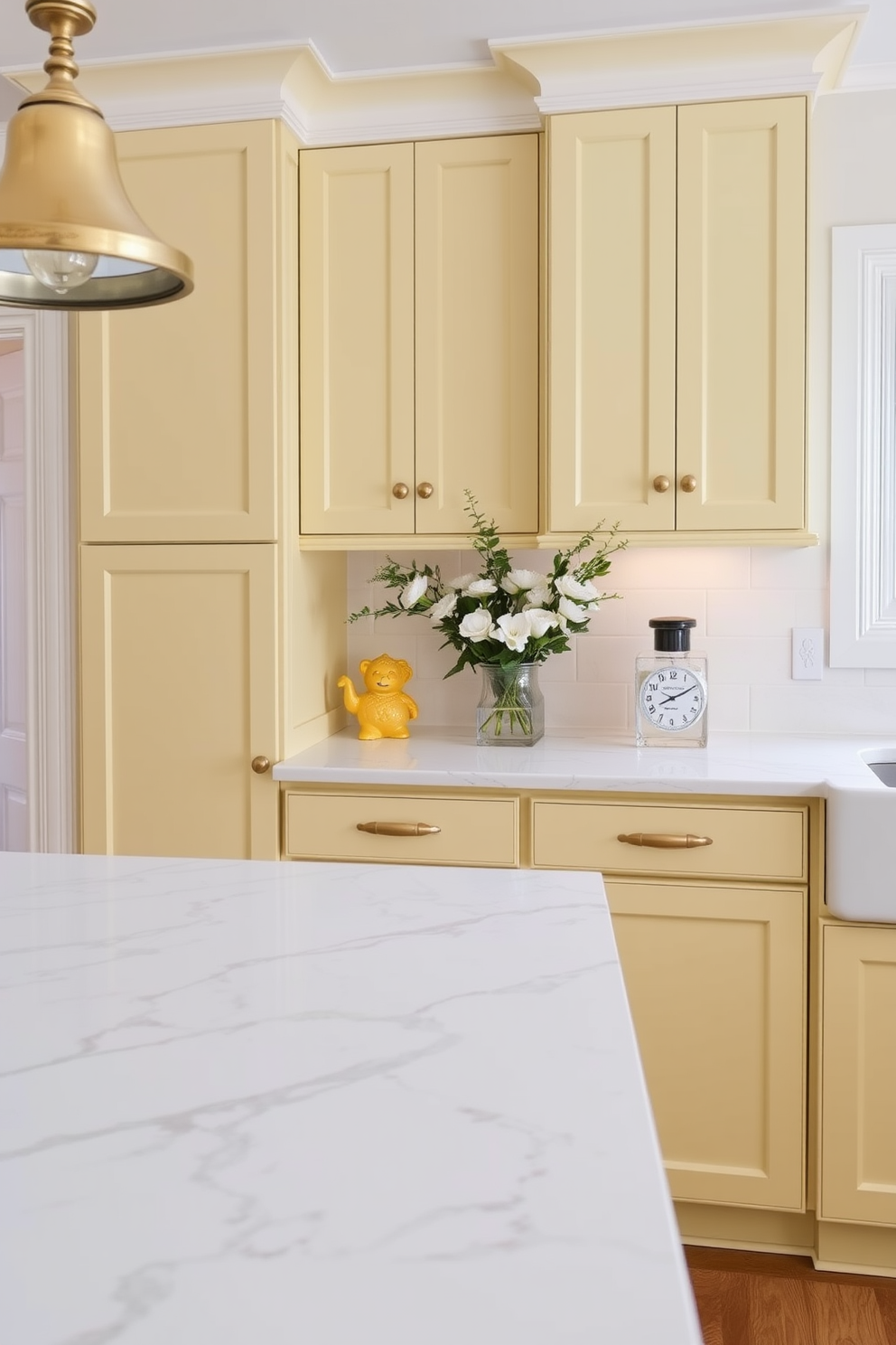 A bright and cheerful kitchen featuring muted yellow cabinetry with elegant brass hardware. The space is enhanced by a white marble countertop that contrasts beautifully with the cabinetry.