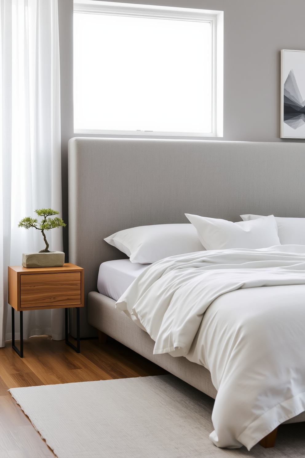 A serene Zen bedroom featuring soft gray walls and a matching gray upholstered bed with plush white bedding. Natural light filters through sheer curtains, illuminating a minimalist nightstand with a simple bonsai tree and a small stone sculpture. The floor is adorned with a light gray area rug that adds warmth to the space. A low wooden dresser complements the room, and a single piece of abstract art in varying shades of gray hangs above it.